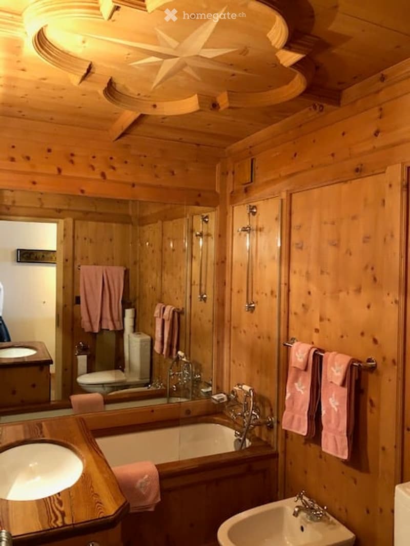 Wooden-paneled bathroom with a large mirror, bathtub, sink, toilet, and pink towels.
