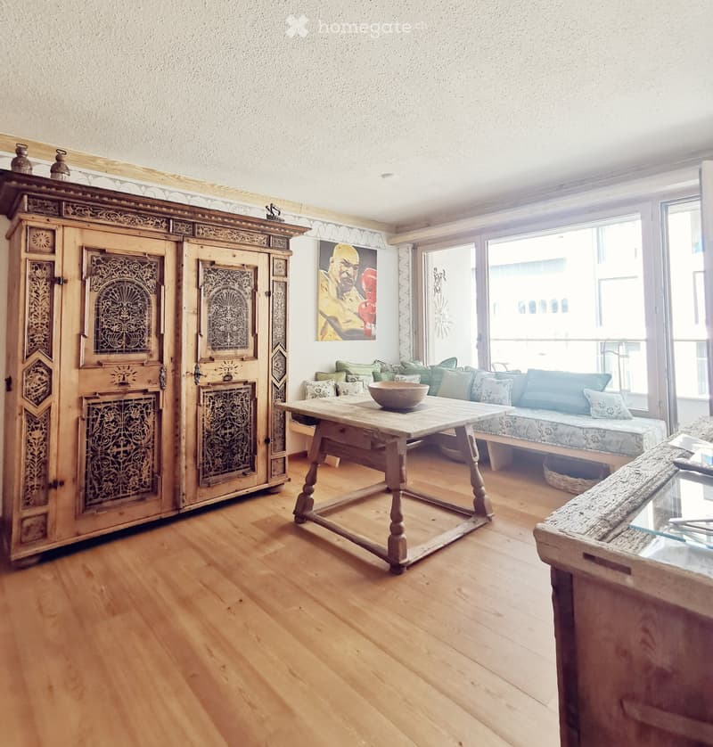 Living room with wooden floor, large window, sofa, coffee table, and ornate wooden cabinet.