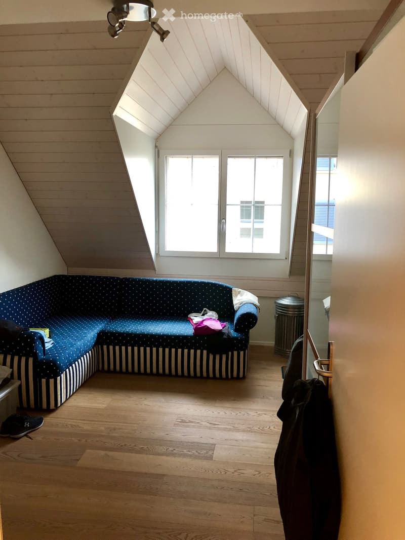 Loft-style room with wooden floors, slanted ceiling, large window, and a blue upholstered sofa.