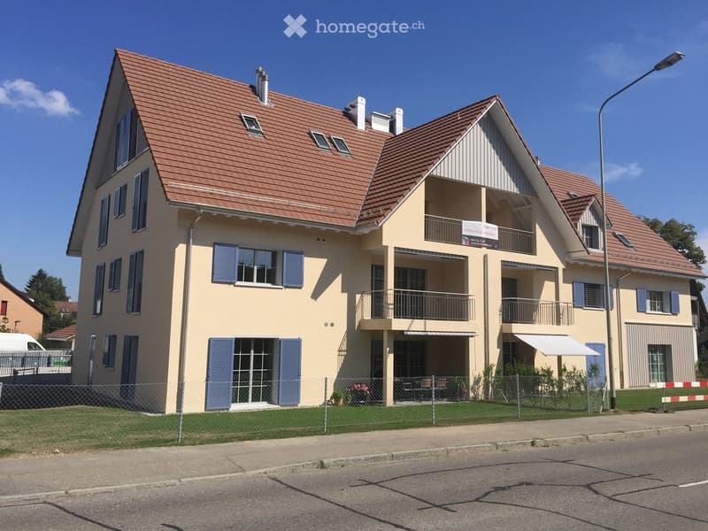 Two-story house with beige walls, red tile roof, multiple windows with blue shutters, balconies, and a fenced front yard.