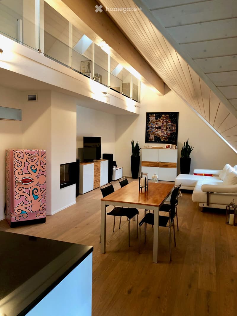 Open-plan living and dining area with wooden flooring, a white sofa, a wooden dining table with chairs, a television, a colorful refrigerator, and decorative plants.