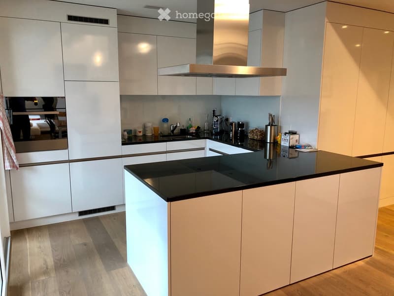 Modern kitchen with white cabinets, black countertop, and stainless steel appliances. Features a central island with built-in lighting, a sink, and various kitchen items on the counter.