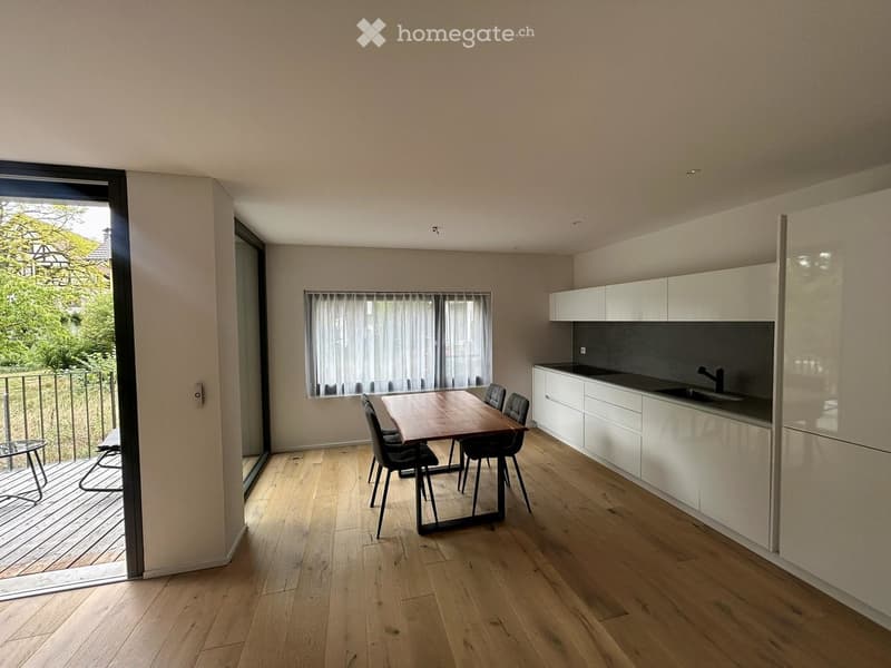 Open-plan dining and kitchen area with light wood flooring, white cabinets, a wooden dining table with four chairs, and a modern kitchen sink.