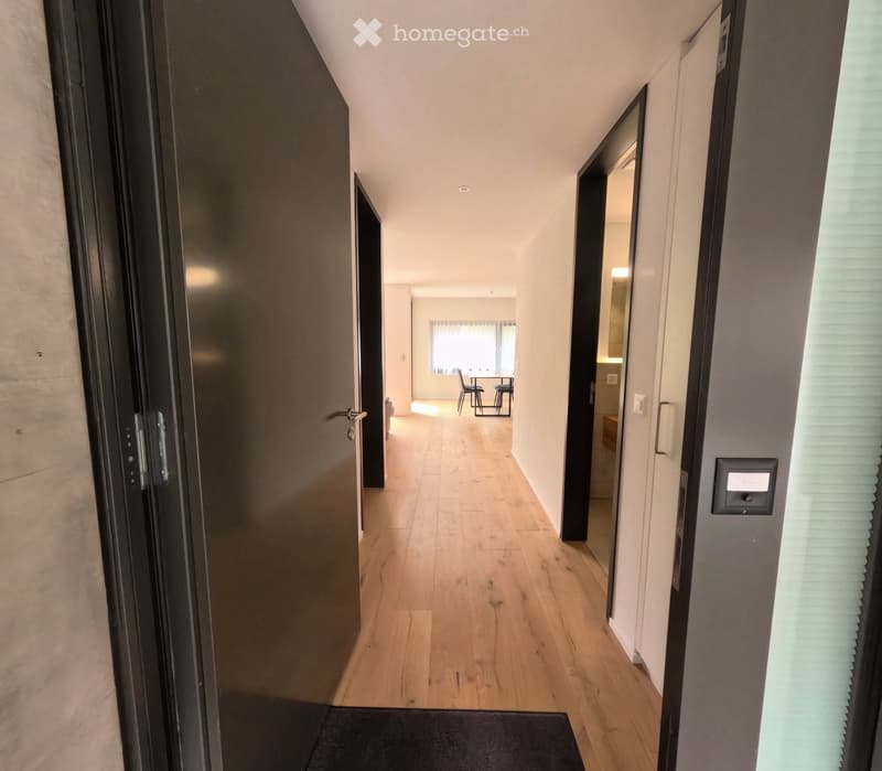 A modern hallway with wooden flooring, white walls, and several doors leading to different rooms, including a dining area and a bathroom.