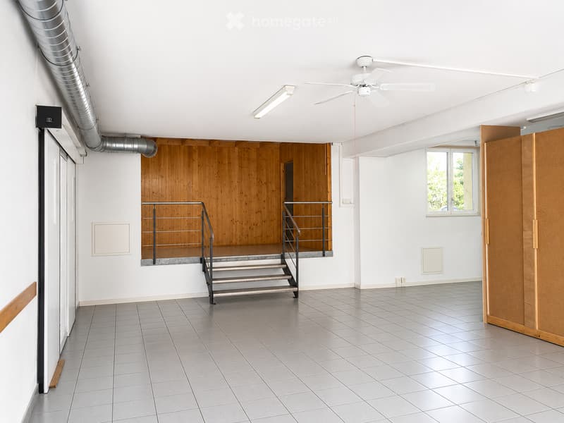Empty room with tiled floor, white walls, wooden paneling on one wall, staircase leading to an upper level, and a window letting in natural light.