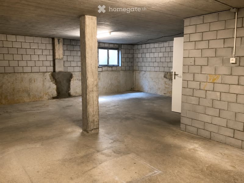 Empty room with exposed brick walls, concrete floor, and a single window. No furniture or equipment present.