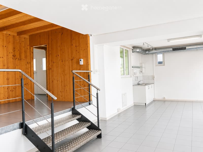 Empty room with white tiled floor, wooden wall, staircase with metal railing, and small sink area with white cabinet.