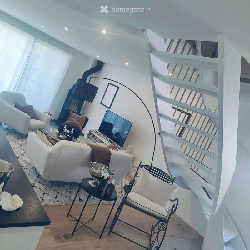 Modern living room with white walls, wooden floor, large windows, spiral staircase, sofa, chairs, coffee table, and decorative items.