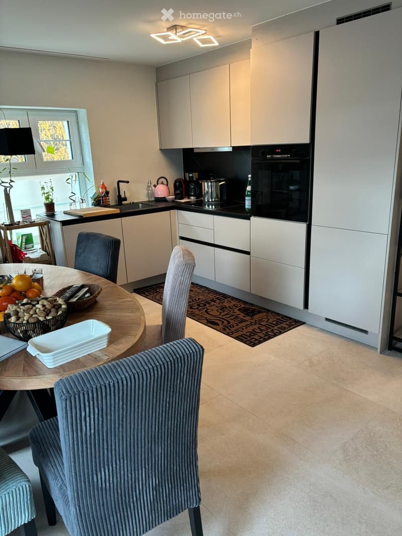Modern kitchen with white cabinets, tiled floor, black countertops, and built-in appliances such as an oven and a dishwasher.