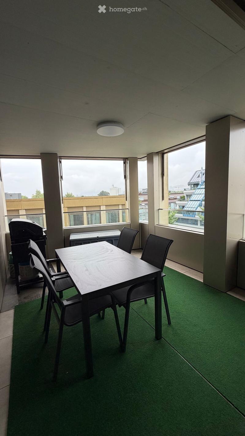Balcony with green artificial turf, a small table with four chairs, and a grill on the left side.
