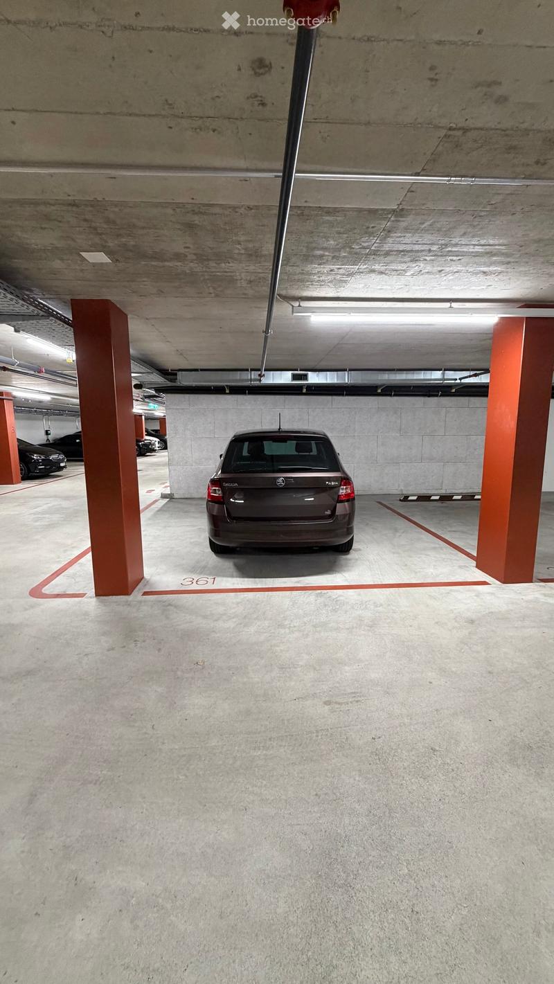 Underground parking area with concrete floors and pillars, marked parking spaces, and a parked car.