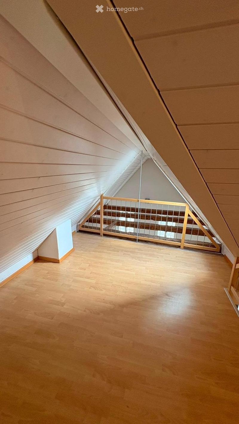 Empty attic space with wooden flooring, slanted wooden ceiling, and a staircase leading down, featuring natural light from a skylight.