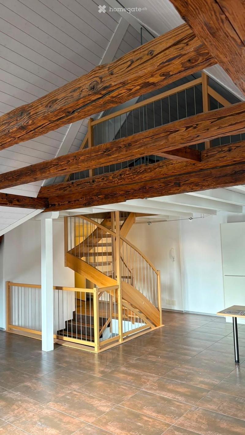 Open hallway with exposed wooden beams and a modern staircase featuring a metal railing and wooden steps.