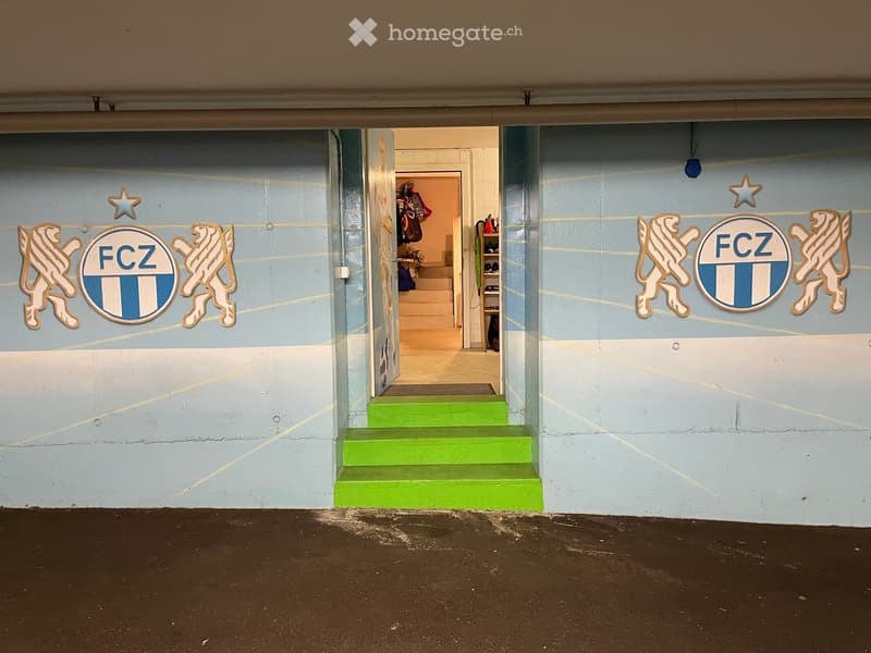 A brightly colored hallway with green stairs leading upwards, featuring FCZ logos and lion emblems on the walls.
