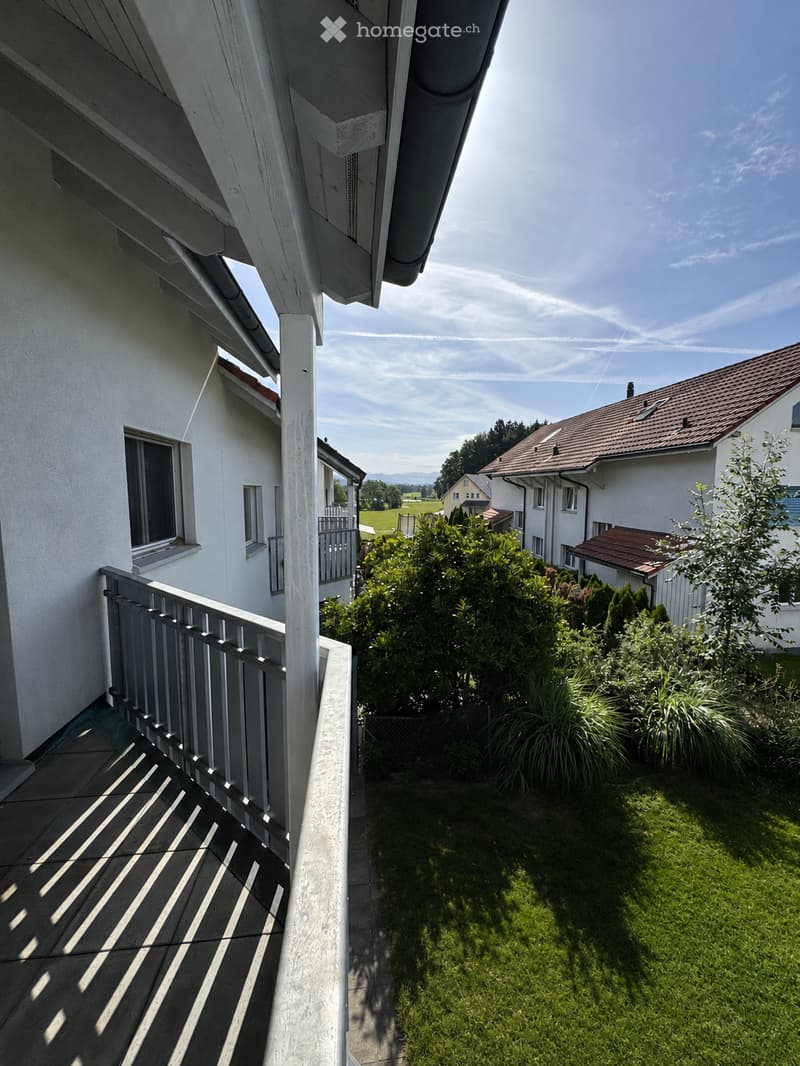 Balcony with metal railing, tiled floor, and view of a well-maintained garden with green grass and bushes.