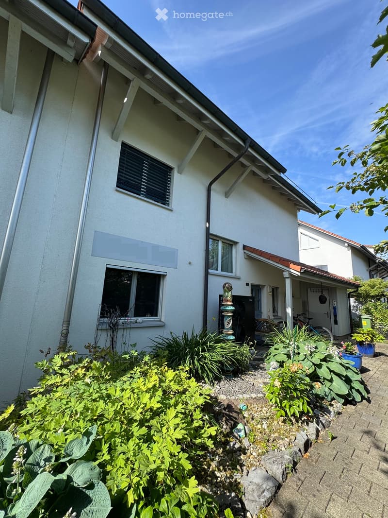 Two-story house with white exterior, multiple windows, and a small garden area with plants and a decorative statue.