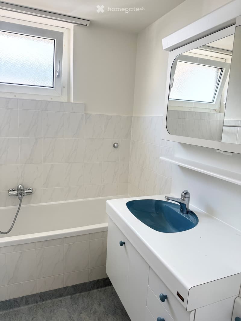 Modern bathroom with a white tiled wall, a bathtub, a sink with a modern faucet, and a mirrored cabinet above the sink.