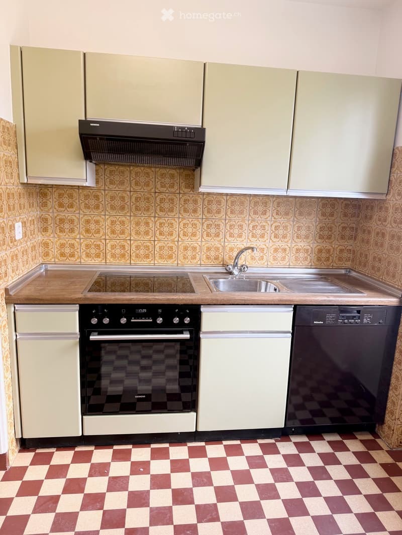 Kitchen with light-colored cabinets, a wooden countertop, a stainless steel sink, a faucet, a black oven, and a dishwasher. The floor has a red and white checkered pattern, and the walls are tiled with a floral pattern.