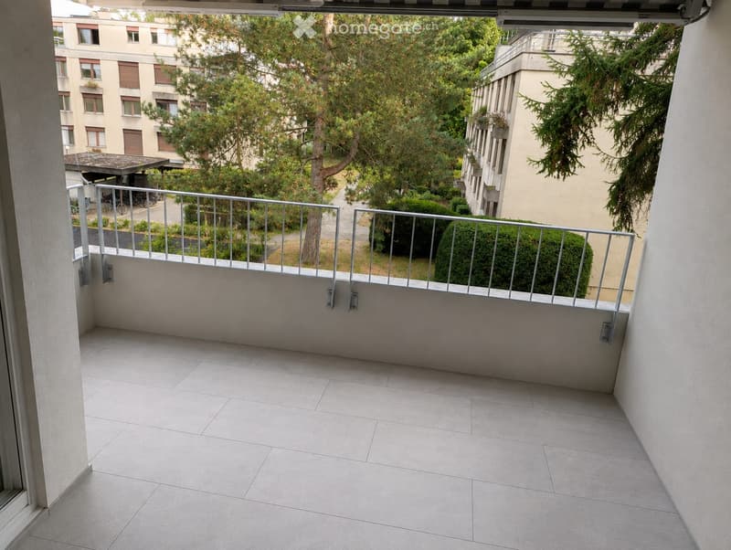 Balcony with tiled floor, metal railing, and view of greenery and buildings.
