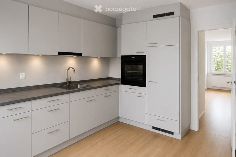 Modern kitchen with white cabinets, stainless steel sink, and built-in oven. Light wooden flooring and sleek design.