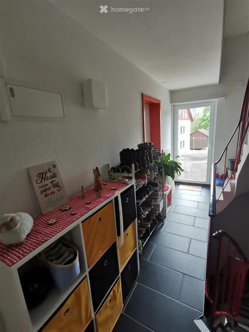 Corridor / Hallway. A narrow hallway with a shoe rack, a small shelf with decorative items, and a view of the outdoor area through a glass door.
