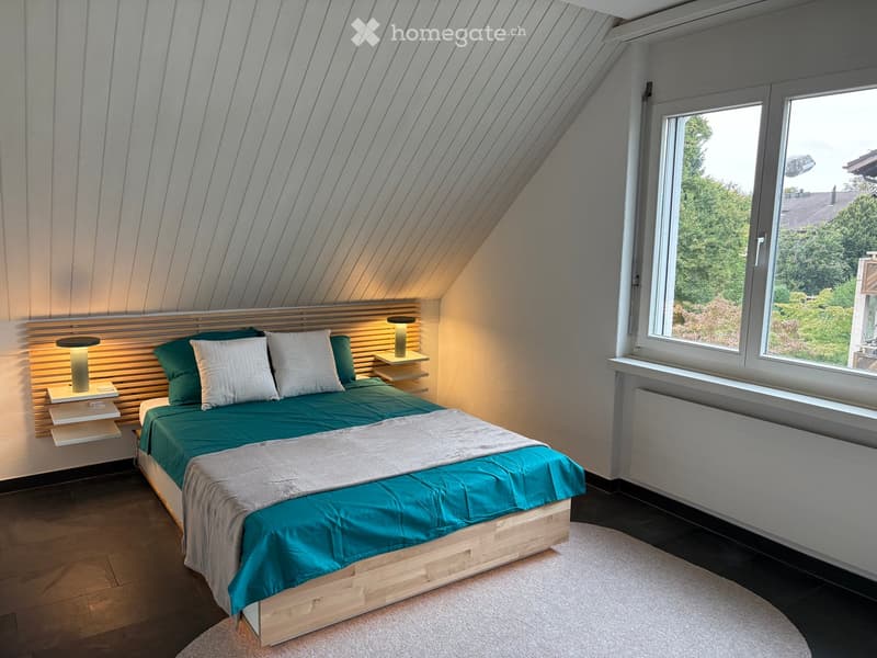 small room with wooden bed, wooden shelves with lamps, round carpet, window with view
