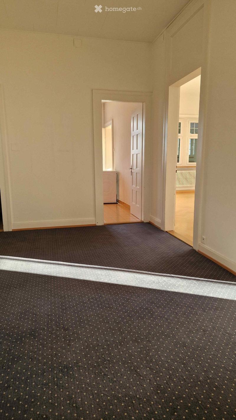 Empty room with white walls, wooden floor, and carpeted floor, two doors, and windows