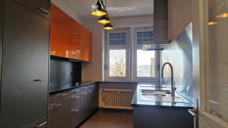 modern kitchen with orange cabinets, stainless steel sink, black countertops, white radiator, large windows with view