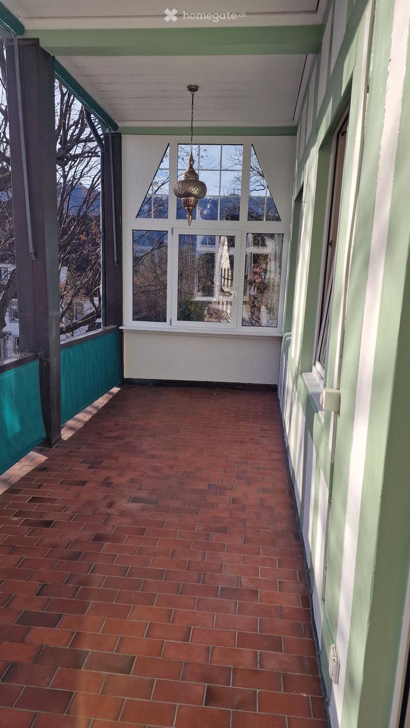 Balcony with red brick floor, green railing, large windows, chandelier
