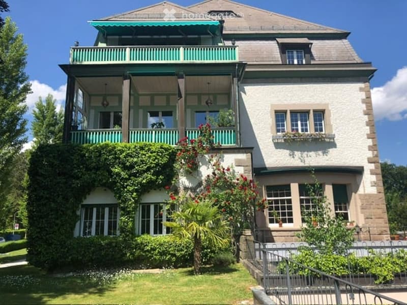 2 story house, white walls, green trim, balcony, garden, red flowers, green plants