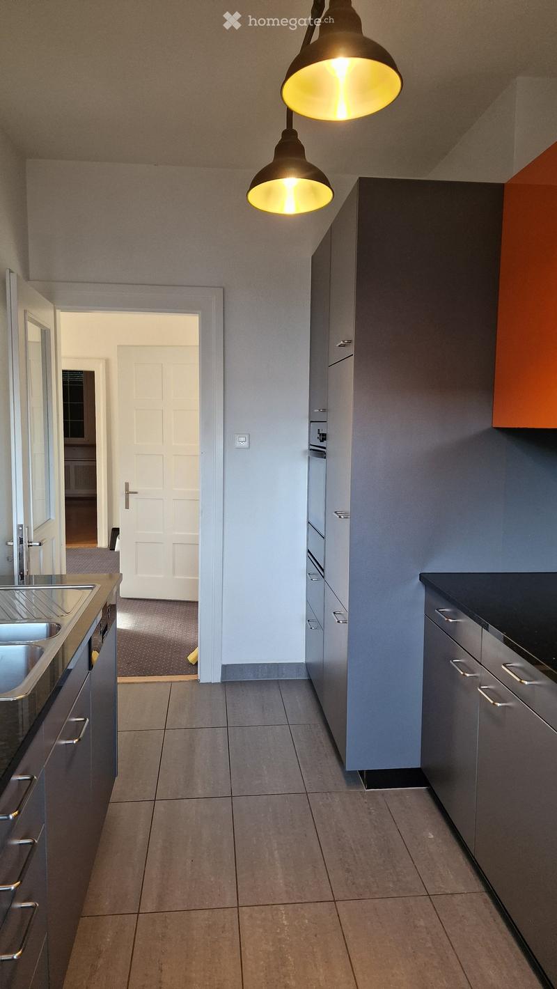 modern kitchen with gray cabinets, black countertops, stainless steel sink, two ovens, dishwasher, washing machine