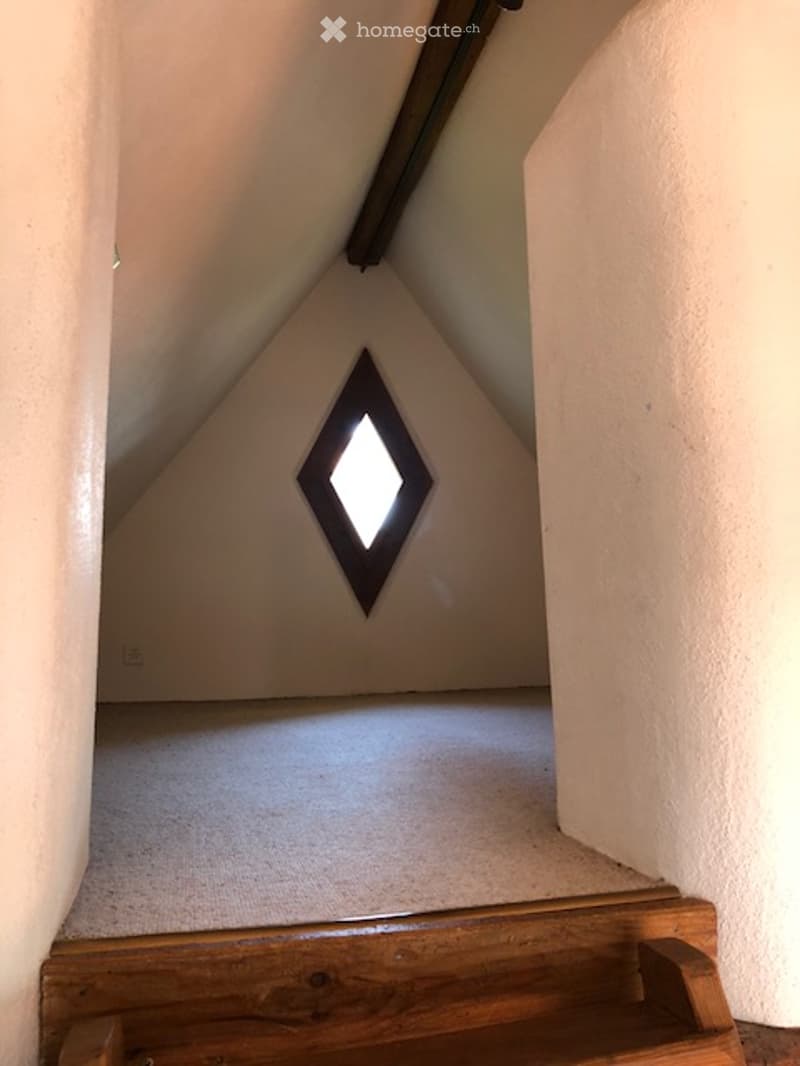An attic hallway with a slanted ceiling, wooden floor, and a diamond-shaped window letting in natural light.
