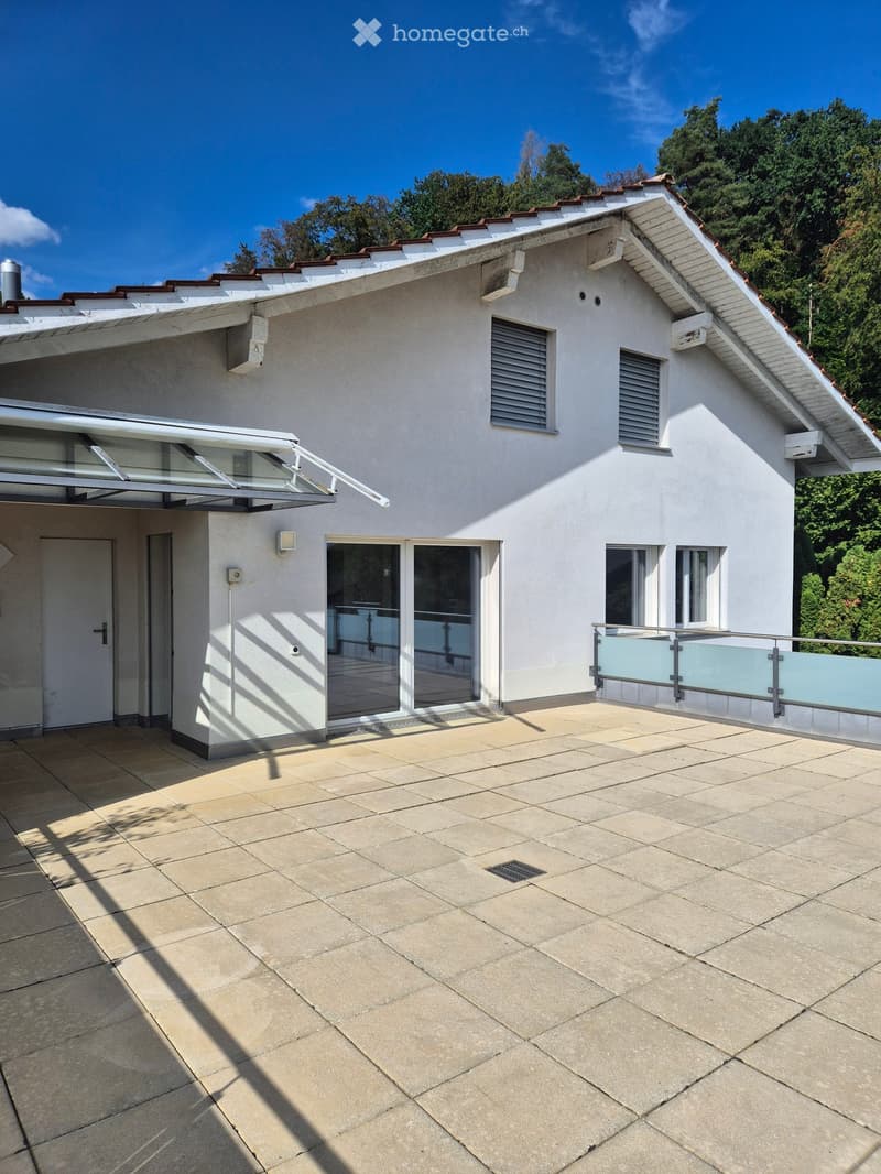 Modern two-story house with white exterior, red-tiled roof, large windows, and a covered entrance area.