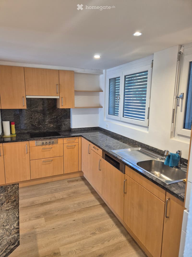 Modern kitchen with light wooden cabinets, granite countertops, stainless steel sink, and built-in appliances.