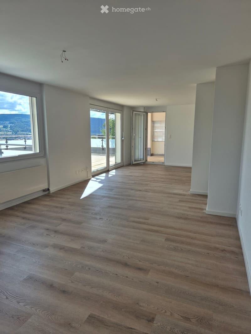 Empty room with wooden flooring, large windows, and sliding glass doors leading to a balcony.