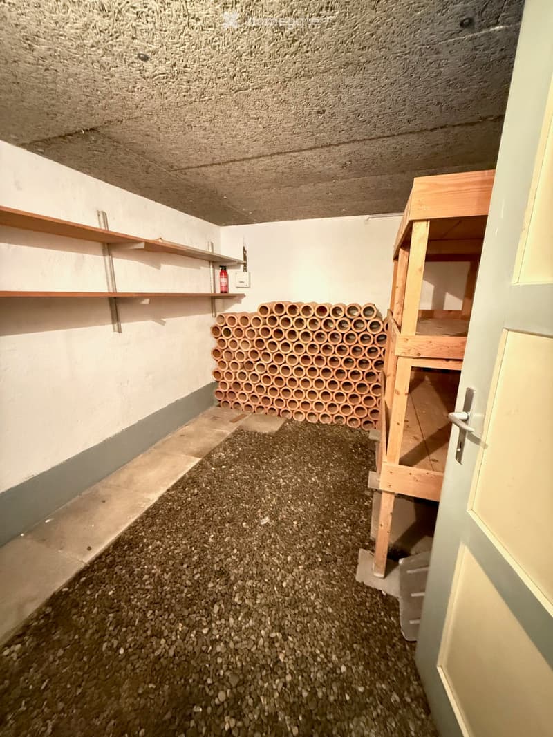 Empty room with concrete walls, wooden shelves, and a stack of plastic tubes on the floor.