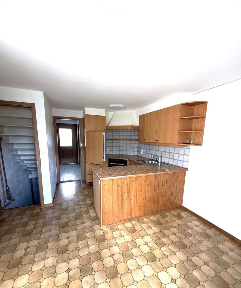 Empty kitchen with wooden cabinets, a countertop, sink, and oven. Hexagonal tiled floor and white walls.