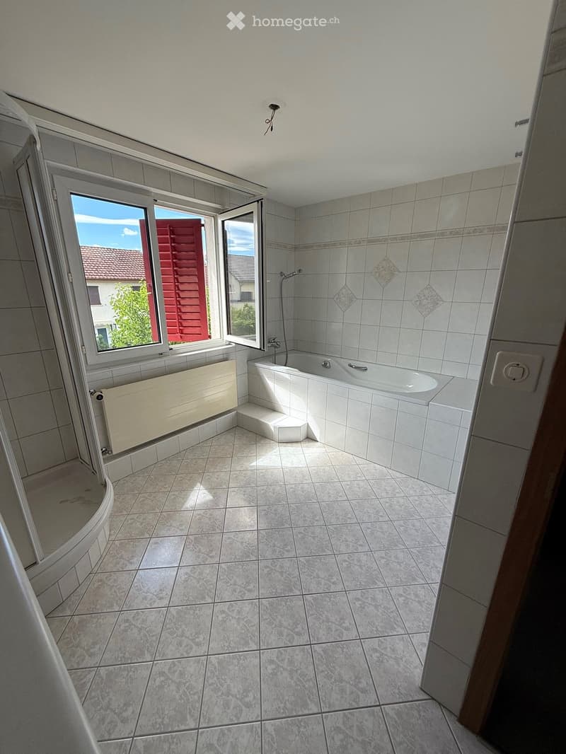 Bathroom with a bathtub, tiled walls and floor, radiator, and a window offering a view of the outside.