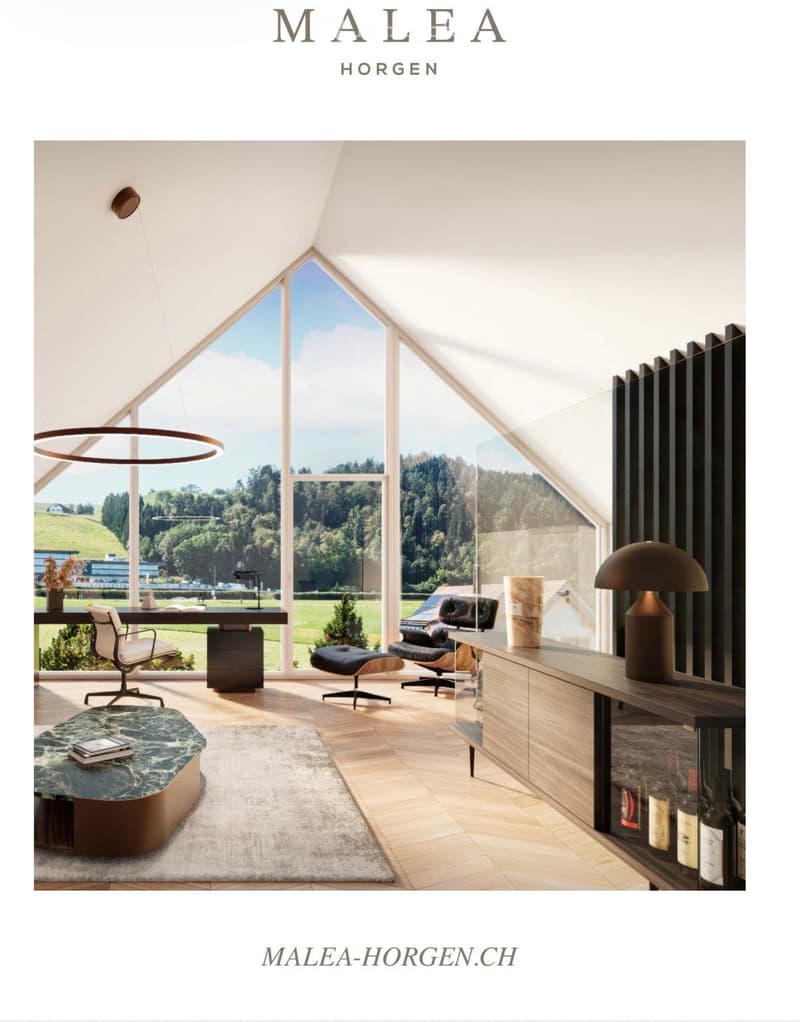Modern, high-ceilinged room with large windows offering a scenic view, featuring a desk, chairs, a round table, lamps, and a shelf with bottles.