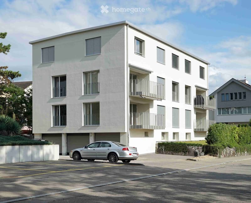 Modern two-story white building with multiple windows and balconies, a parked car in front, and surrounding greenery.