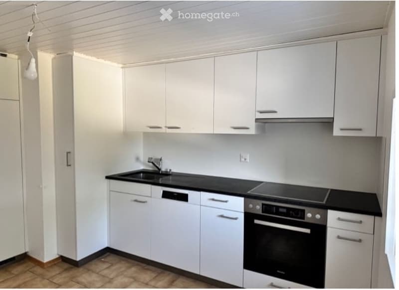 Modern kitchen with white cabinets, black countertops, and built-in appliances including a sink, oven, and dishwasher.