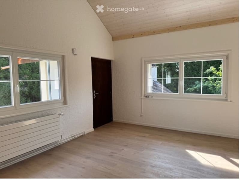 Empty room with wooden flooring, white walls, large windows, and a single door. No furniture or equipment present.