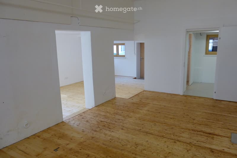 Empty room with wooden flooring and white walls, featuring open doorways leading to other rooms.