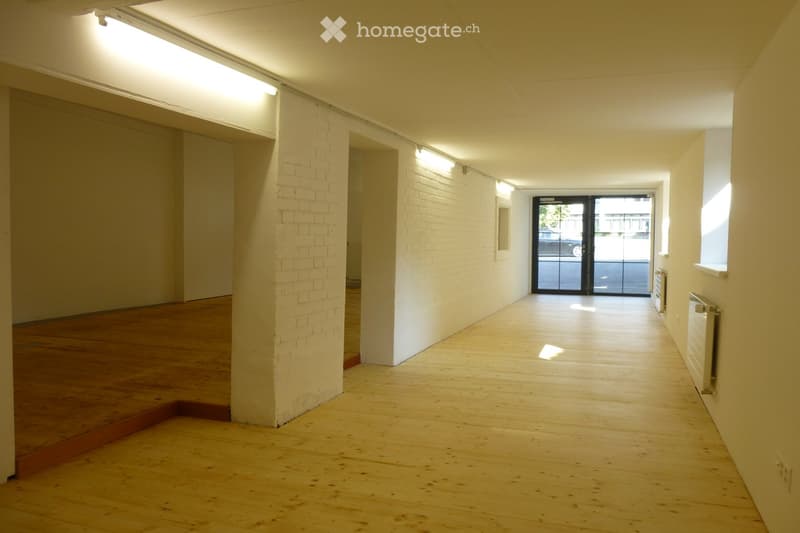 Empty hallway with wooden flooring, white brick walls, and a large glass door at the end leading to an outdoor area.