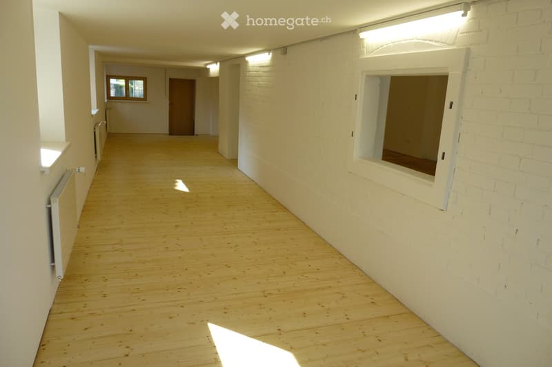 Empty hallway with wooden flooring, white brick walls, and recessed lighting. Features a window and a door at the far end.