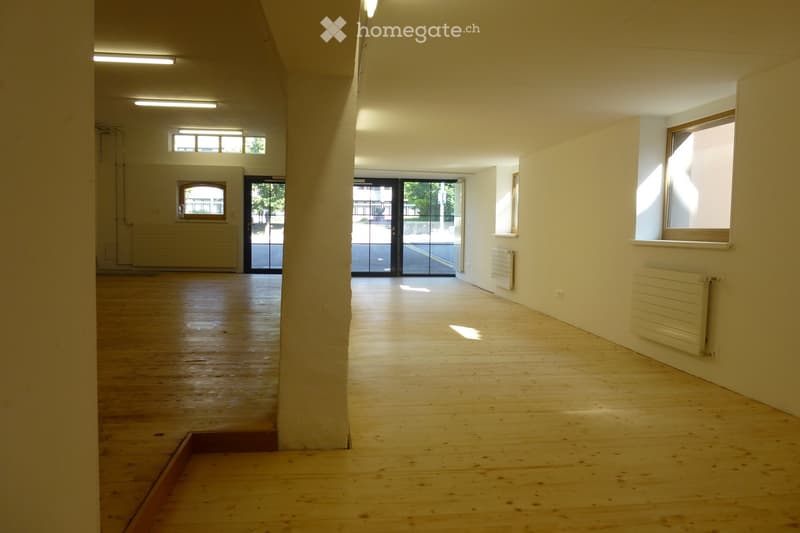 Empty room with wooden flooring, white walls, and large windows allowing natural light. No furniture or equipment present.