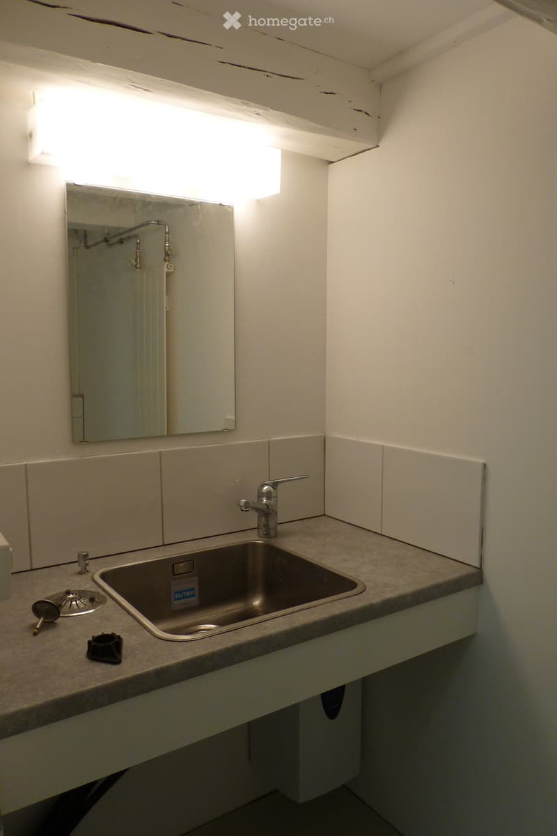 Bathroom with a sink, faucet, and mirror. The sink has a sticker on it, and there are some small items on the counter.