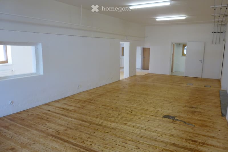 Empty room with wooden flooring and white walls, featuring several doorways leading to other spaces.