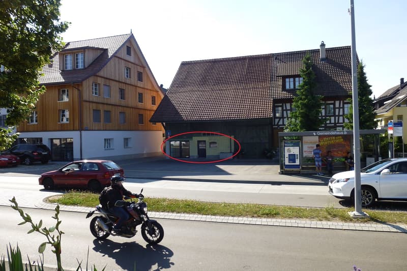 Two-story residential buildings with pitched roofs, multiple windows, and a small garage. A motorcycle rider is passing by on the road.
