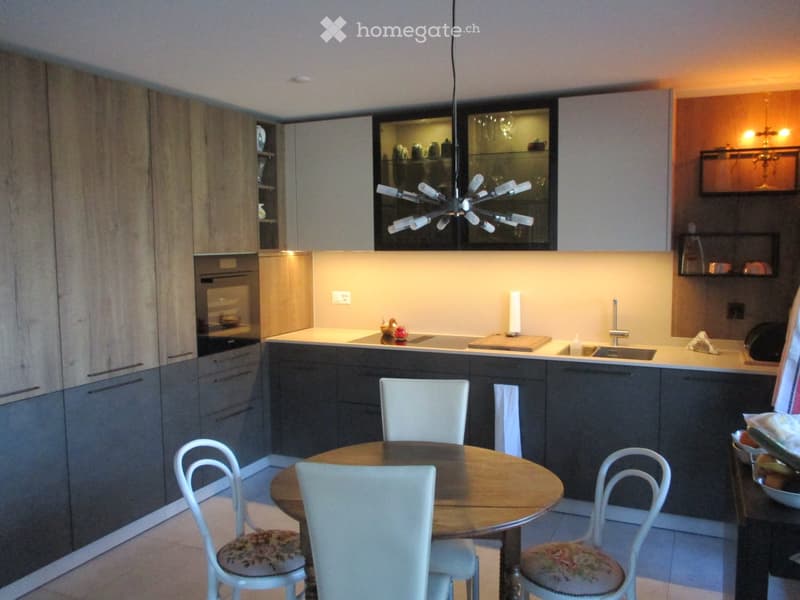 Modern kitchen with grey cabinets, a central island, a round dining table with four chairs, and a hanging light fixture.